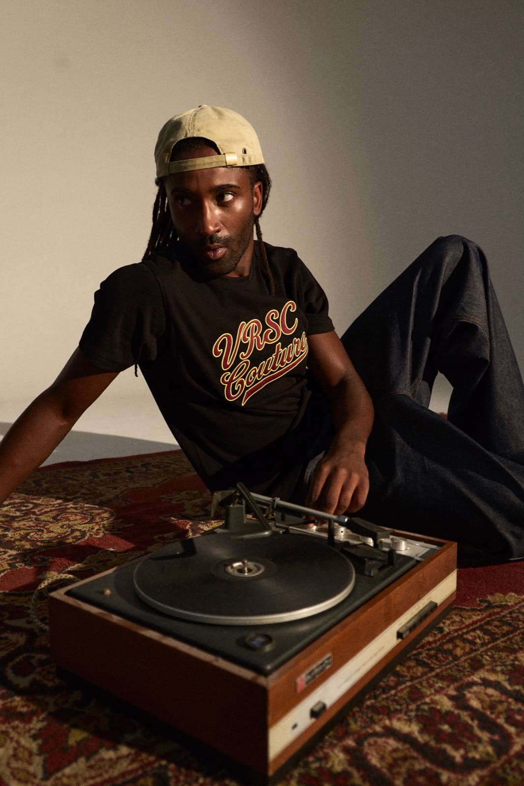 VRSC Couture FW — ragazzo seduto su un tappeto accanto a un giradischi, t-shirt con logo
