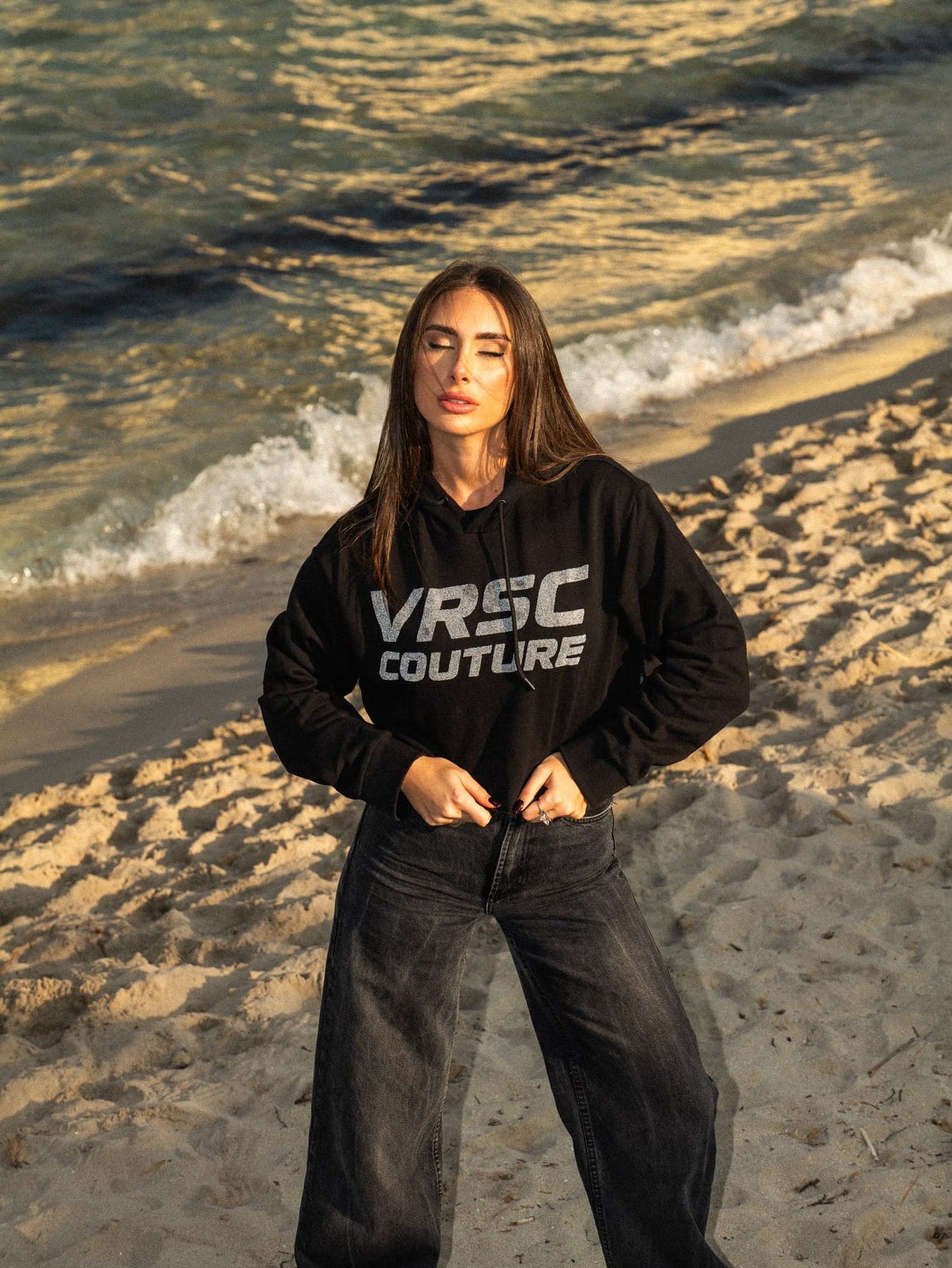 VRSC Couture — modella in felpa nera VRSC Couture sulla spiaggia